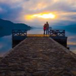 Couple standing on dock looking at sunset