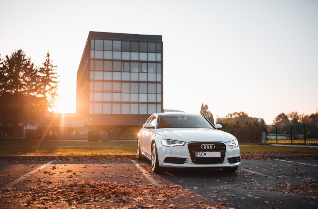 White Audi sedan parked on concrete parking area surrounded by dried leaves